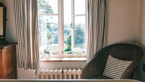 Une pièce avec une fenêtre, un radiateur, une chaise en osier et un meuble en bois.