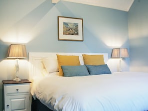 Ein ordentlich gemachtes Bett mit weißer und blauer Bettwäsche, zwei Nachttischlampen, ein gerahmtes Bild an der Wand und ein kleiner Nachttisch mit Schubladen.