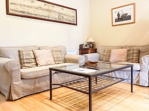 Ein Wohnzimmer mit zwei beigefarbenen Sofas, einem Glastisch und einem gerahmten Stadtbild an der Wand.