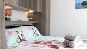 Una camera da letto con testiera in legno, un letto con lenzuola a motivi floreali, due lampade da comodino e un asciugamano arrotolato sul letto.