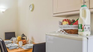 Un'area pranzo con un tavolo apparecchiato per la colazione, un frigorifero con una bottiglia di latte e un cestino con pane e burro.