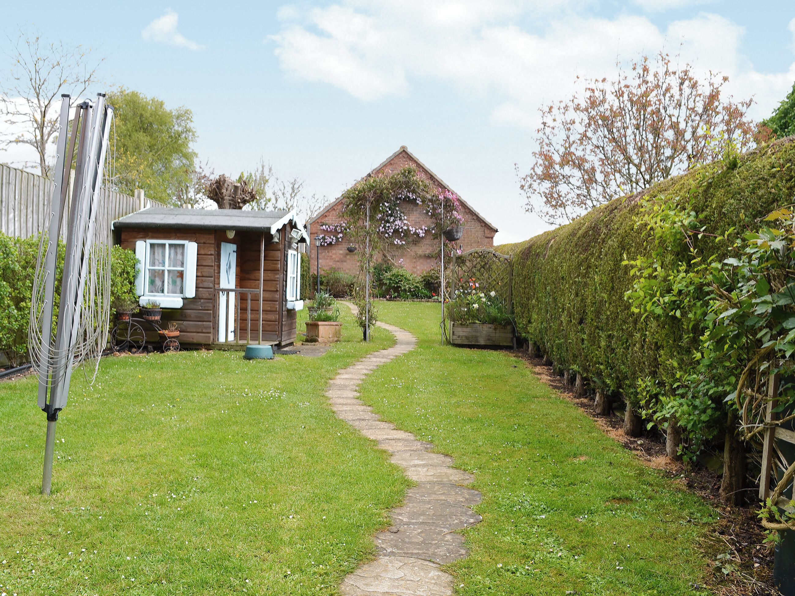 A garden path leading to a wooden cottage with a brick house in the background.