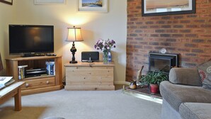 A living room with a flat-screen TV, a lamp, a wooden cabinet, a sofa, and a brick wall.