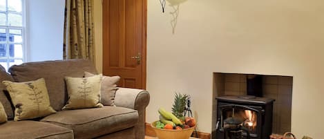 A cozy living room with a sofa, a table with breakfast items, a fireplace, and a window with curtains.