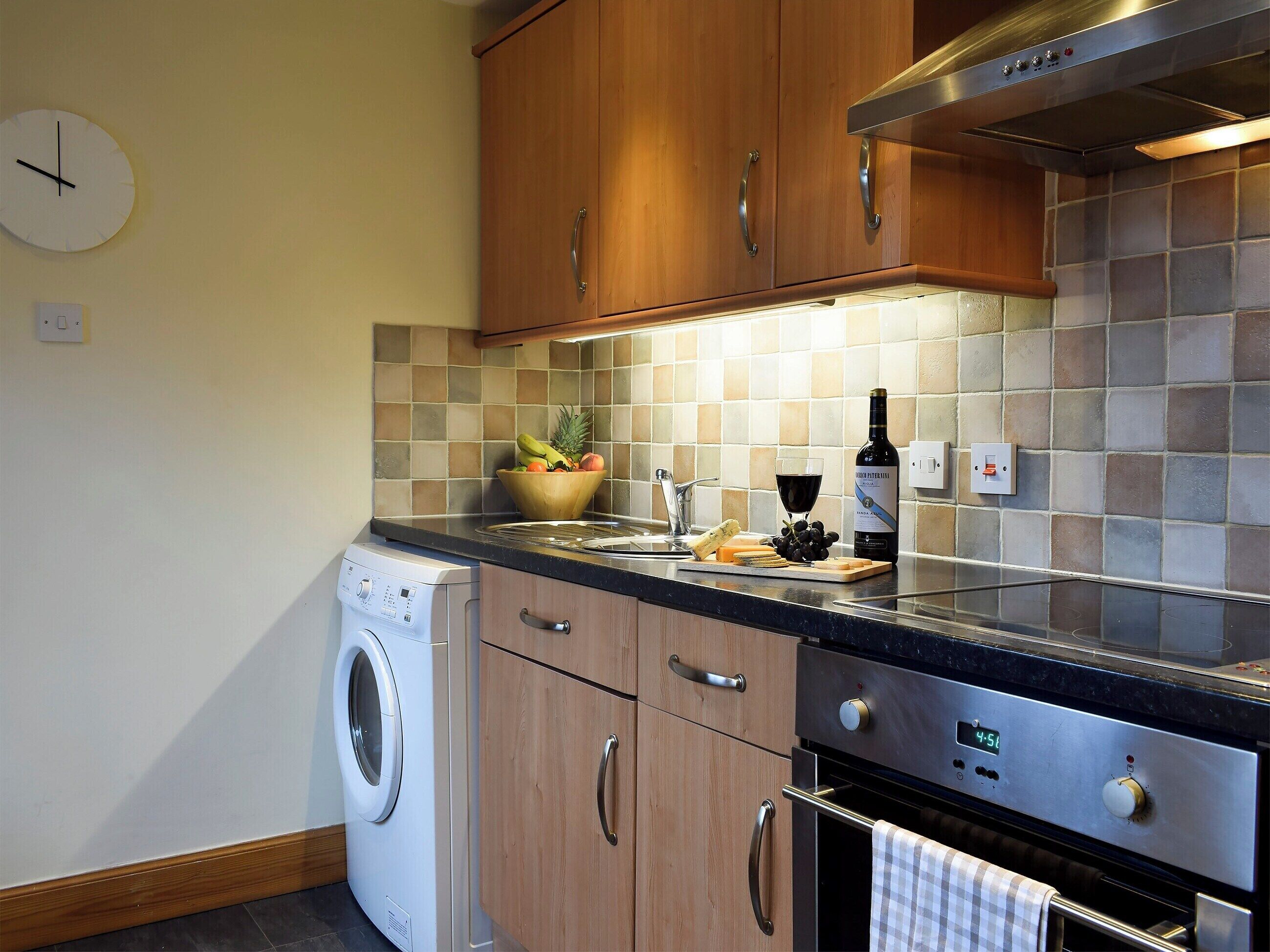 Une cuisine moderne avec des meubles en bois, une hotte de cuisinière en acier inoxydable, un lave-linge et un pare-feu en carrelage.