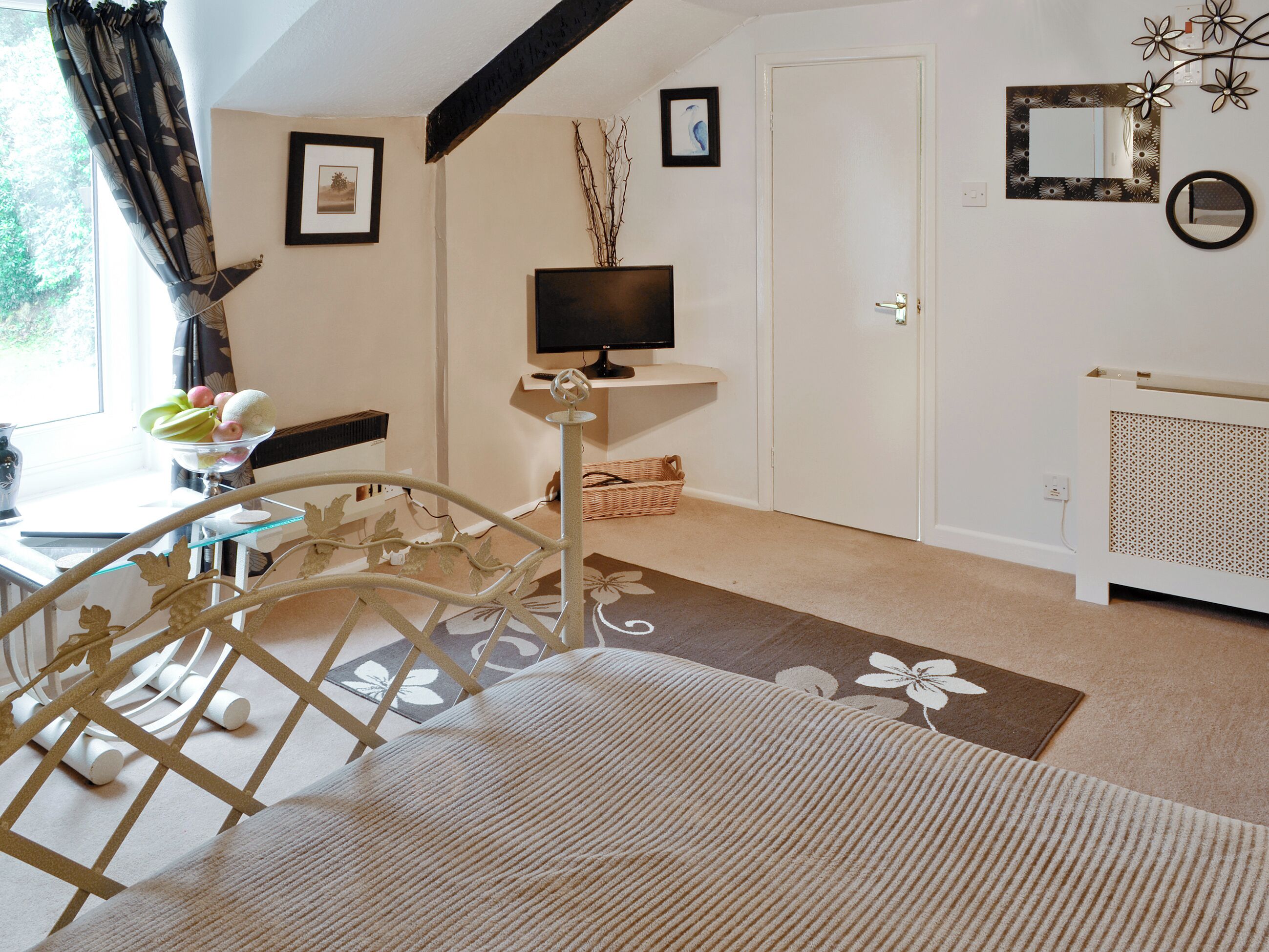 Une pièce comprenant un lit, un bureau, une chaise, un téléviseur et une fenêtre avec des rideaux.