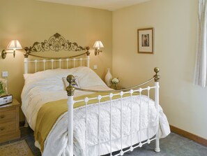 A bed with a white frame and decorative headboard, two bedside lamps, a nightstand with a radio, and a framed picture on the wall.