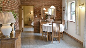 Un comedor con pared de ladrillo, una mesa redonda, sillas de madera, una lámpara y un espejo.