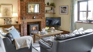Una sala de estar con chimenea, sofás de cuero, televisor y estantería.
