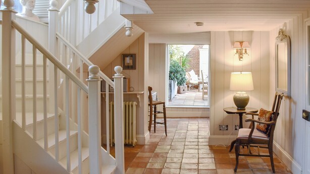 A staircase with white balusters leading to a landing with a table and chairs, a radiator, and a view of an outdoor area with plants and a chair. - 2 bedroom accommodation in Ilketshall St. Margaret, near Bungay (Ilketshall St. Margaret, near Bungay)