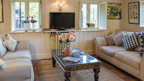 A living room with a sofa, a coffee table, a television, and a window with shutters. - 2 bedroom accommodation in Ilketshall St. Margaret, near Bungay (Ilketshall St. Margaret, near Bungay)