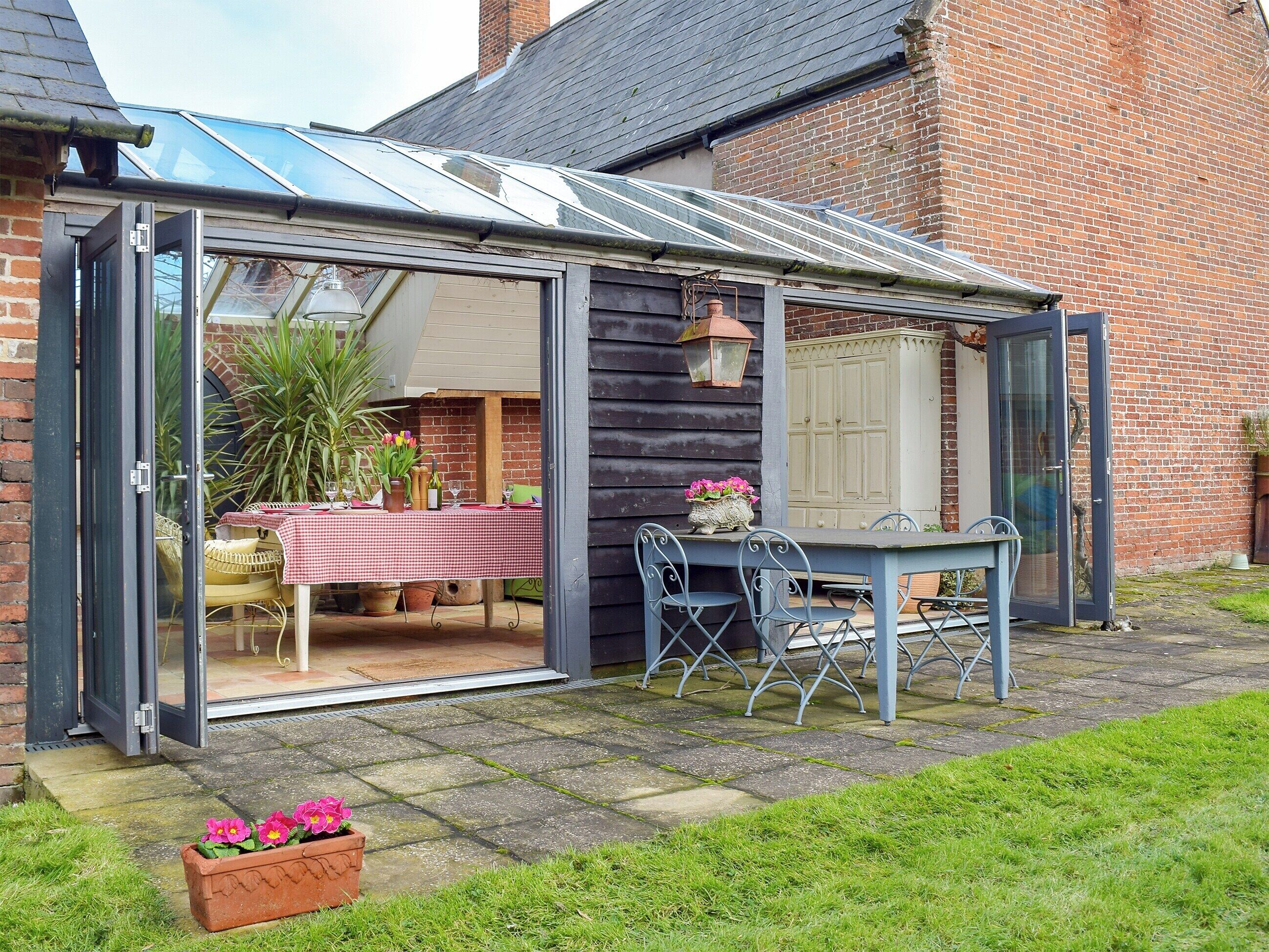 A conservatory with a table and chairs, a potted plant, and a brick wall.