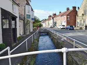 A narrow water channel with a white railing, flanked by buildings including a pharmacy and a church.