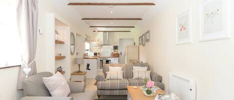 A cozy living room with a sofa, a table with a vase, and a kitchen in the background.