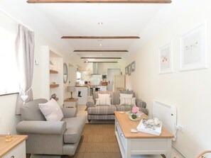 A cozy living room with a sofa, a table with a vase, and a kitchen in the background.