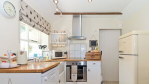 Cocina compacta con microondas, horno y refrigerador. Hay un reloj en la pared y una ventana con cortinas.