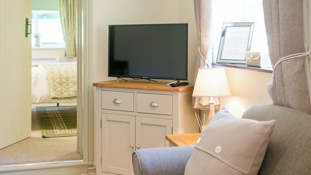 Una habitación con televisión sobre un mueble de madera, un sofá, una lámpara y una ventana con cortinas.