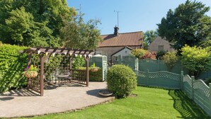 Un jardín con un pérgola, una mesa pequeña y sillas.