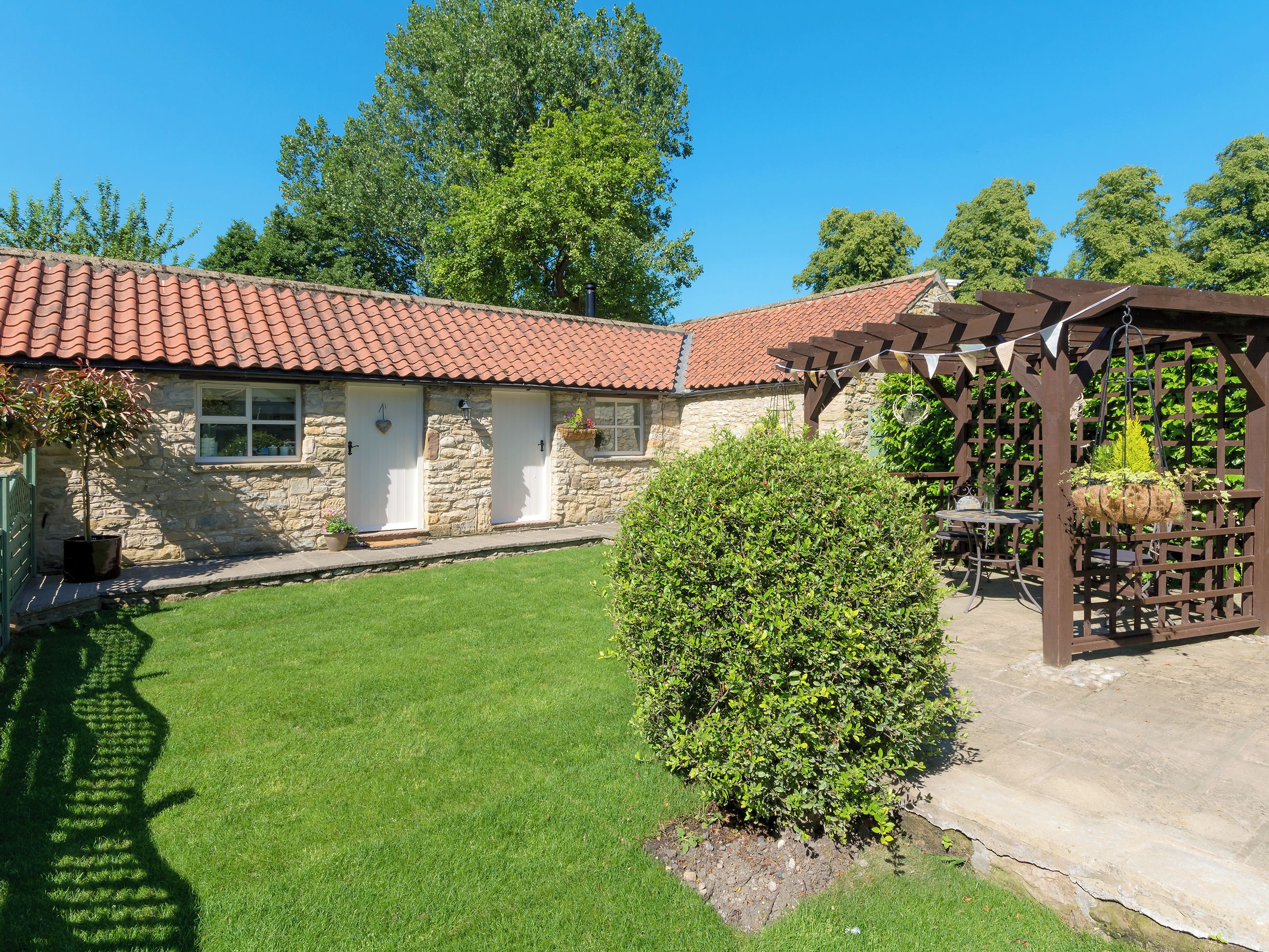 A stone building with a red-tiled roof, a small garden, and a pergola.