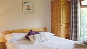 Un lit bien fait, avec du linge de lit blanc, un oreiller violet et un oreiller blanc orné de broderies. Des serviettes pliées sont posées sur le lit. Une armoire en bois se trouve à droite du lit.