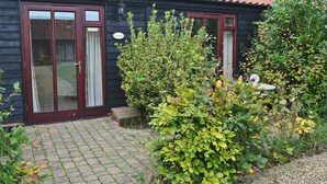 Un chalet en bois avec un toit en tuiles, une porte en bois et un petit jardin agrémenté d’un banc et d’une table.