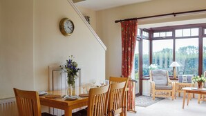 A dining area with a wooden table, chairs, a vase with flowers, and a clock on the wall.