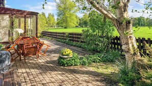 Um pátio com uma mesa e cadeiras de madeira, um jardim com cerca de madeira e uma árvore.