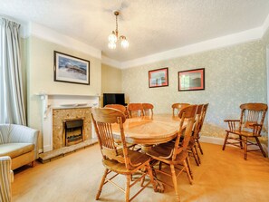 A dining room with a round wooden table, six wooden chairs, a fireplace, and two framed pictures on the wall. - 5 bedroom accommodation in Keswick (Keswick)