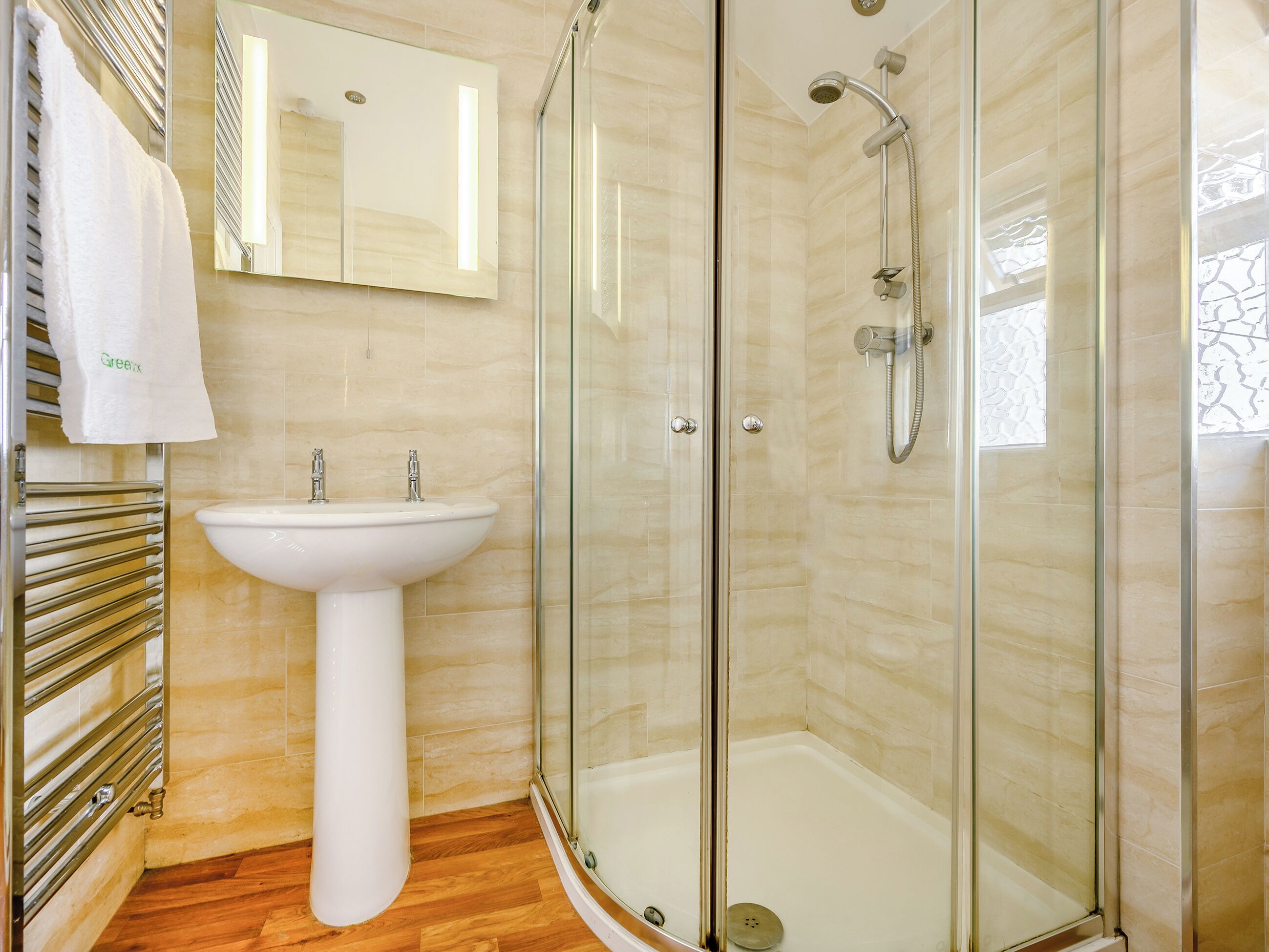 A modern bathroom with a glass-enclosed shower, a pedestal sink, and a towel rack.