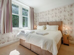 A neatly made bed with pillows and folded towels, a bedside table with a lamp, and a window with curtains.