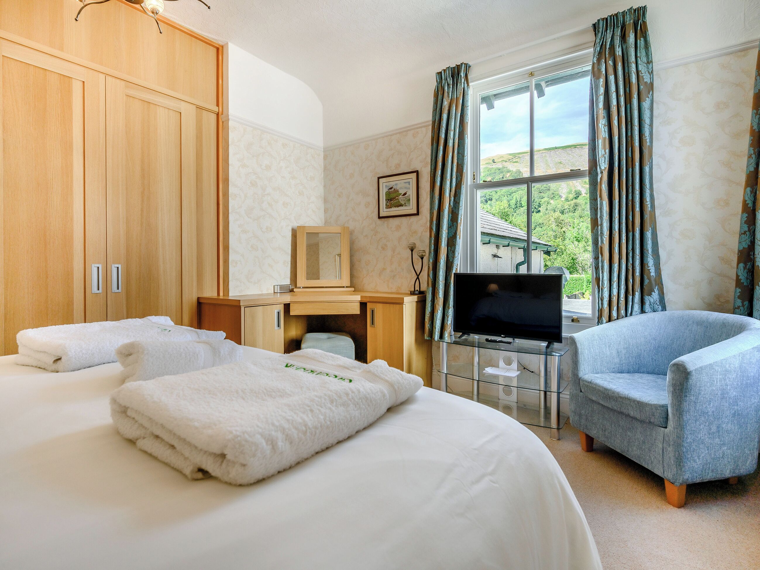 A hotel room with a bed, a desk with a TV, a chair, and a window with curtains.