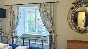 Un dormitorio con cama, ventana con cortinas, espejo y cómoda.