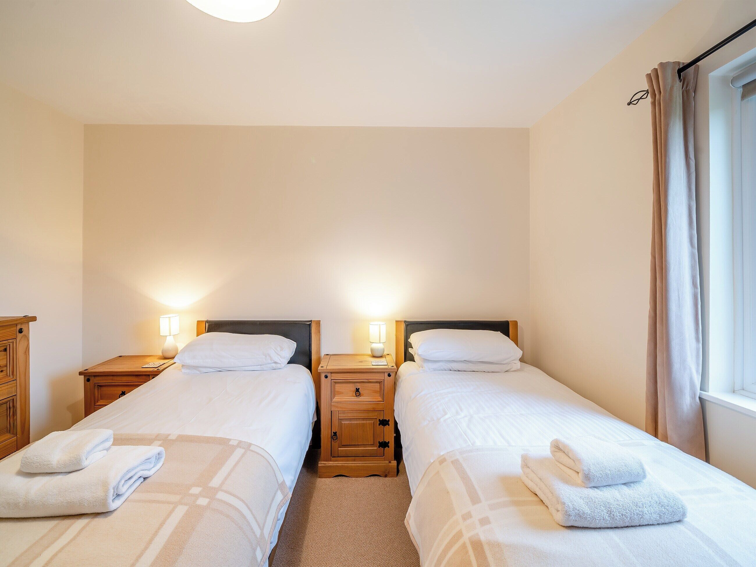 A twin room with two beds, bedside tables with lamps, and a window with curtains.