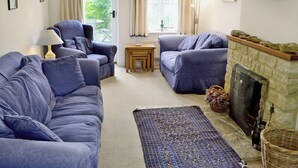 A living room with two sofas, a small table, a fireplace, and a view through the window. - Meadow Cottage-E1793 (Broadwindsor)