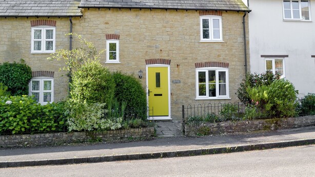 A stone house with a yellow door, white windows, and a thatched roof. - Meadow Cottage-E1793 (Broadwindsor)
