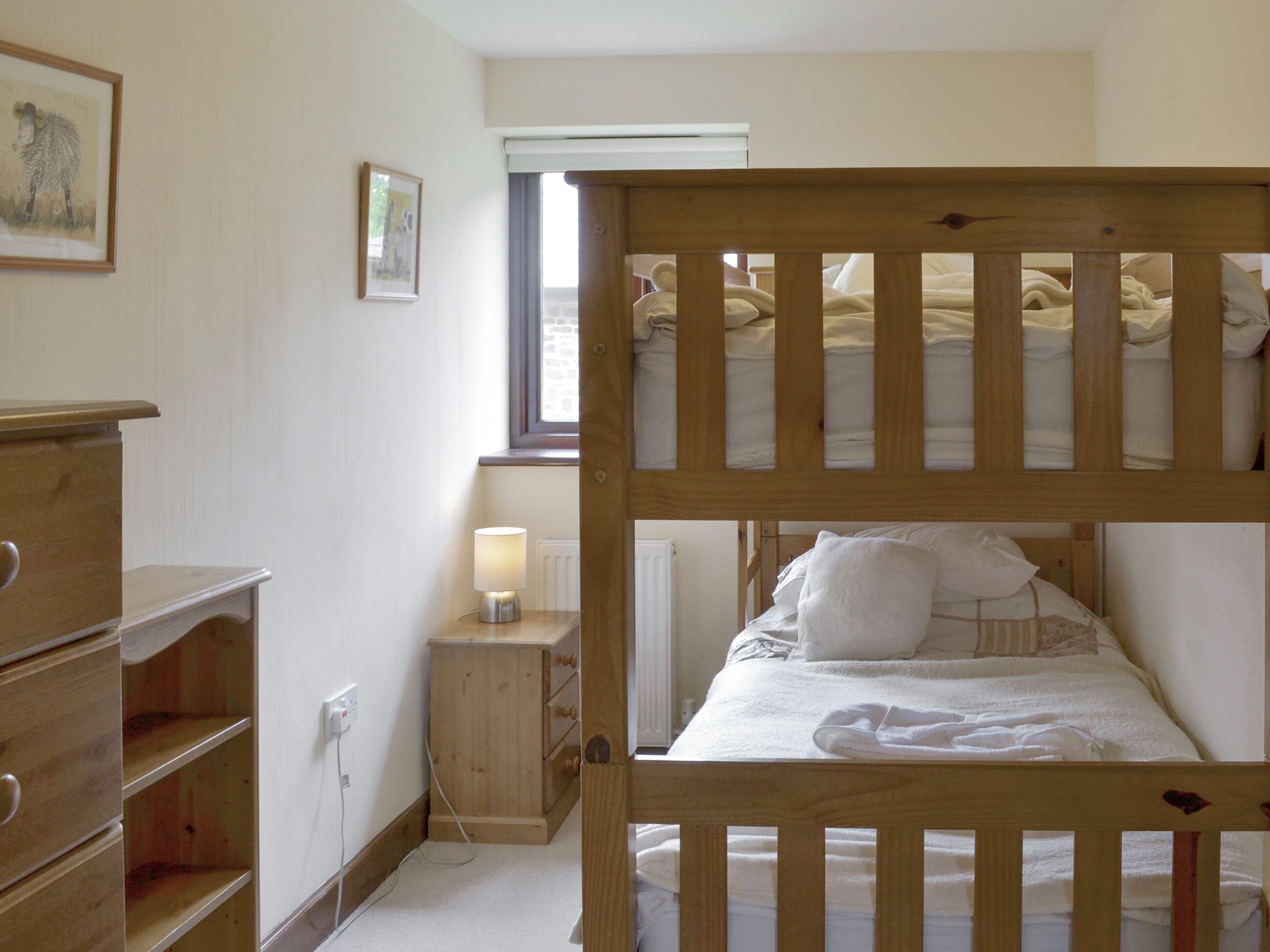A room with a bunk bed, wooden dresser, bedside lamp, and a window with curtains.