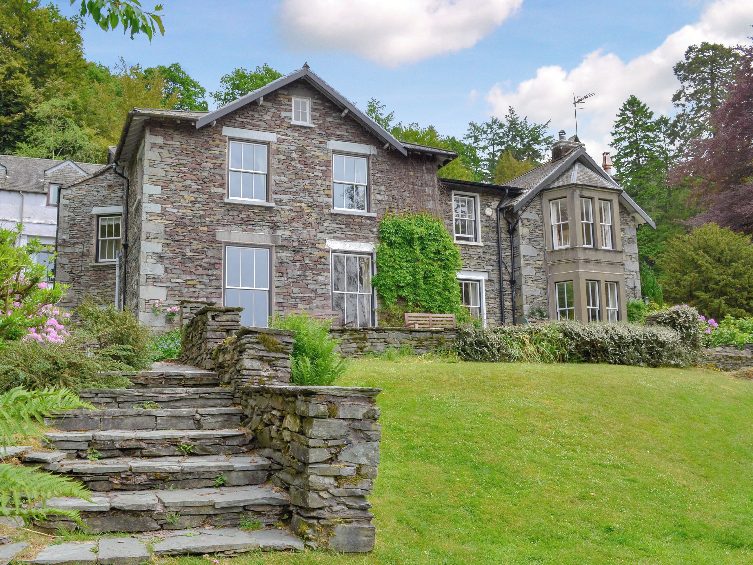 A stone house with multiple windows and a stone staircase leading to the entrance.