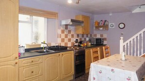 Une cuisine avec des meubles de rangement en bois, une cuisinière, un four à micro-ondes et une table à manger recouverte d’une nappe à motifs floraux.