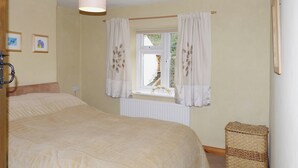 Une chambre avec un grand lit, une fenêtre avec des rideaux, un radiateur et un petit panier en osier.