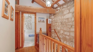 Una escalera de madera que lleva a una habitación con paredes de piedra, una bañera y cuadros enmarcados en la pared.