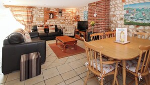 Una sala de estar con pared de piedra, chimenea, televisor y comedor con sillas y mesa de madera.