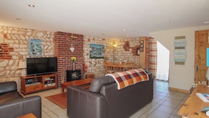 Una sala de estar acogedora con pared de piedra, chimenea, televisión y comedor.