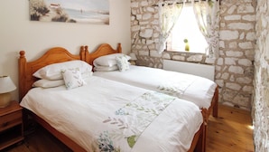 Un dormitorio con dos camas individuales, cabecero de madera, pared de piedra, ventana con cortinas y un cuadro en la pared.