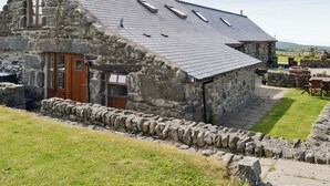 Un edificio de piedra con techo inclinado, una puerta de madera y un muro de piedra que rodea la propiedad.