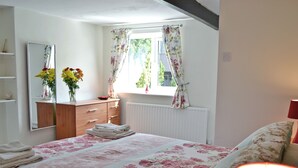 Um quarto com uma cama, cômoda, espelho, janela com cortinas florais e um radiador.