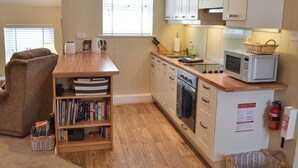 Una cocina compacta con encimeras de madera, microondas, tostadora y una estantería llena de libros.