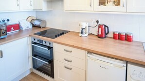 Uma cozinha moderna com armários brancos, forno embutido, cafeteira e chaleira.