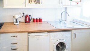 Uma cozinha com armários brancos, cafeteira, chaleira, recipientes para chá e açúcar, pia e máquina de lavar.