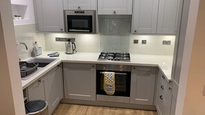 A compact kitchen with grey cabinets, a built-in microwave, a gas stove, and a stainless steel sink. - 2 bedroom accommodation in Keswick (Keswick)