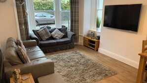 A modern living room with a grey sofa, a wooden coffee table, and a large TV on the wall. - 2 bedroom accommodation in Keswick (Keswick)